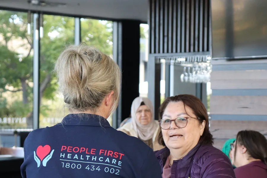 A People First Healthcare team member greeting an older woman at a community centre