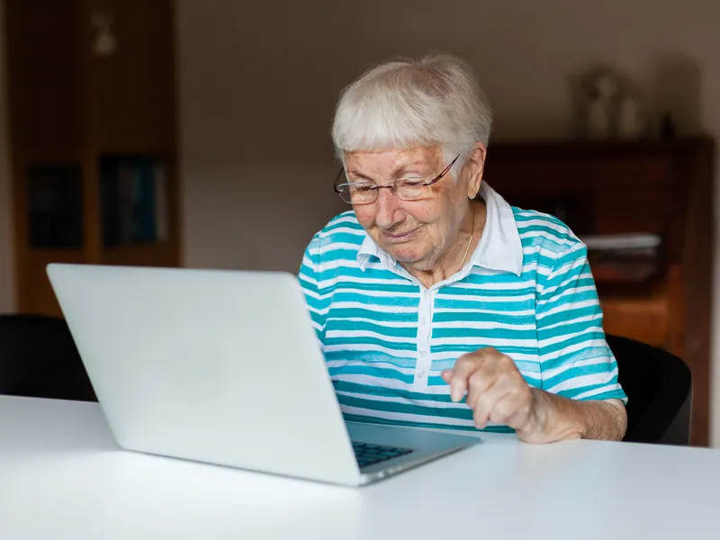 An older woman using a laptop at her kitchen table