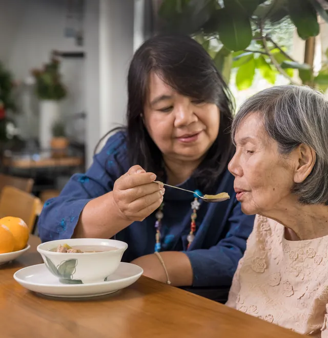 A carer supporting an older woman on a walk outdoors