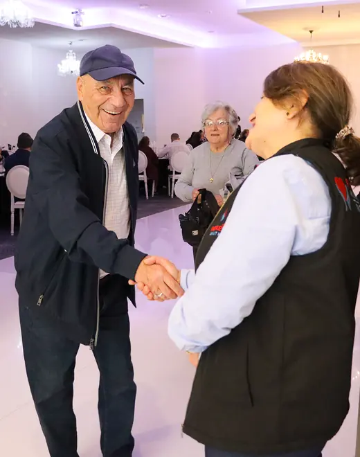 A People First Healthcare team member shaking hands with a smiling older man at a community lunch