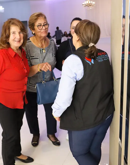 A People First Healthcare team member in a branded vest talking with two older women at a community event