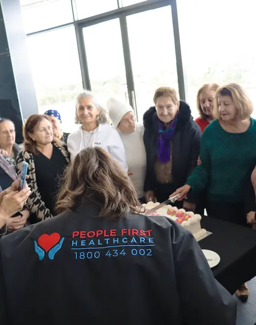 A People First Healthcare team member cutting a celebration cake with a group of older women
