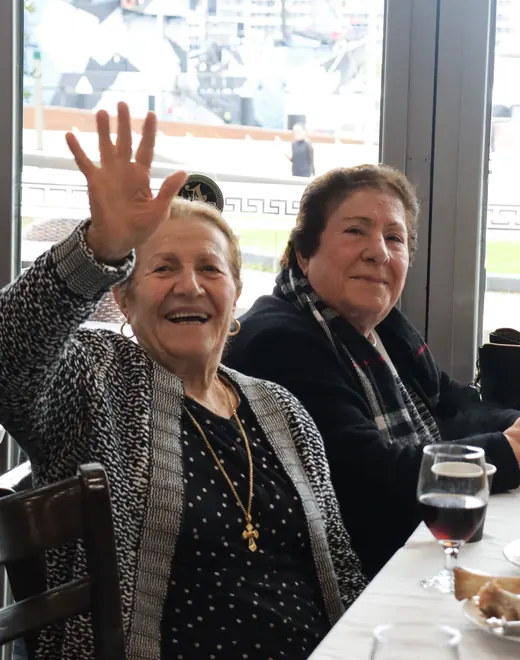 Two older women seated together at a People First Healthcare group outing, one waving at the camera