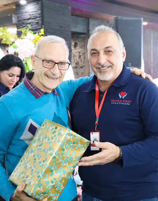 A People First Healthcare team member with an arm around an older man holding a wrapped gift