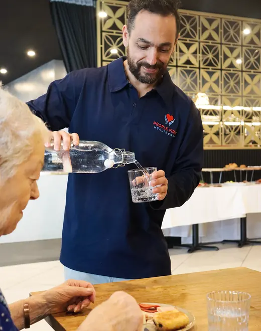 A People First Healthcare team member pouring a glass of water for an older woman at a table