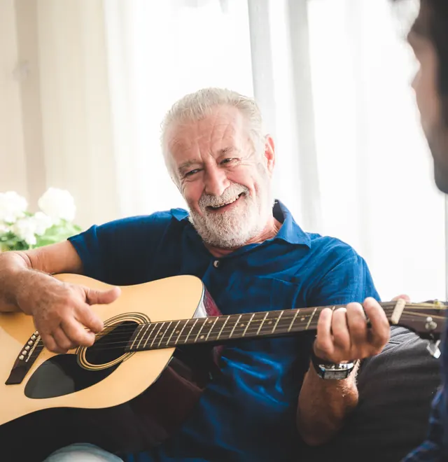 An older man playing guitar while a People First Healthcare carer listens