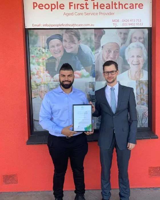 Two People First Healthcare staff outside the first shopfront, holding a framed certificate