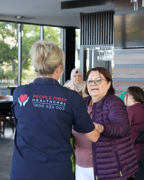 A People First Healthcare carer greeting an older woman at a community gathering