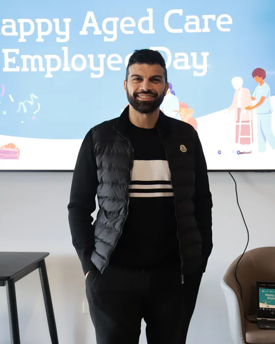 A People First Healthcare team member in front of an Aged Care Employee Day screen at the office